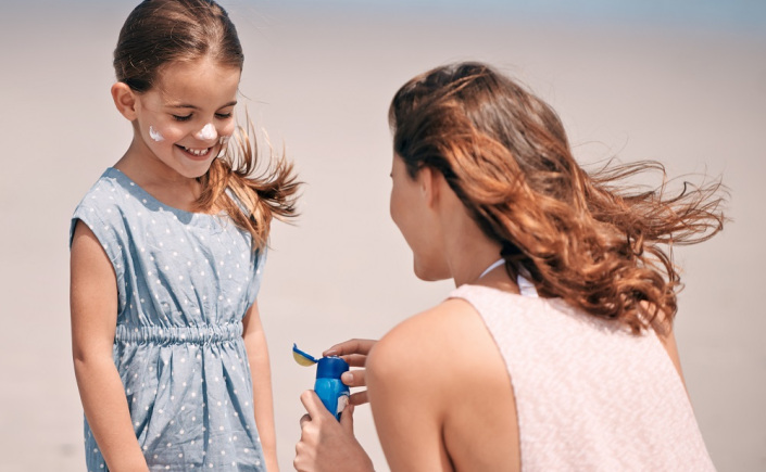 mãe passando protetor na filha como proteger as crianças do sol