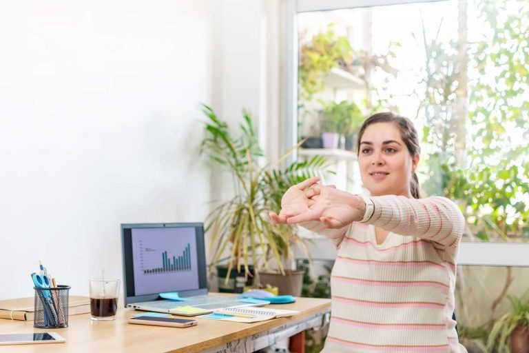 mulher sentada em cadeira de escritório alongando os braços para melhorar a postura no trabalho